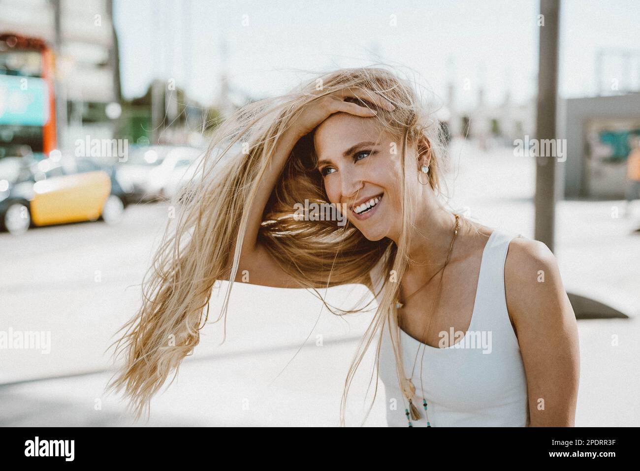 Portrait d'une jeune femme souriante tenant ses cheveux dans la ville Banque D'Images