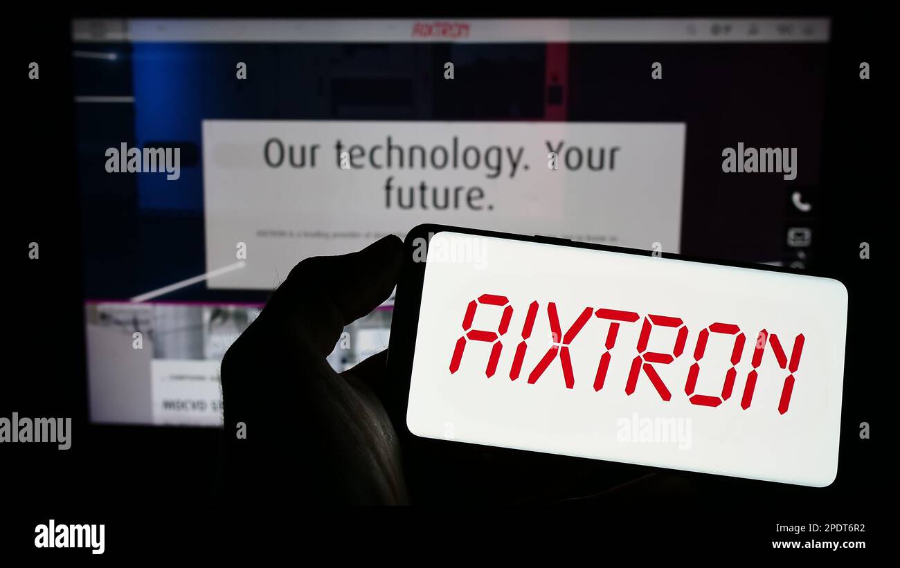 Personne tenant le téléphone portable avec le logo de la société allemande de technologie Aixtron se sur l'écran en face de la page web d'affaires. Mise au point sur l'affichage du téléphone. Banque D'Images