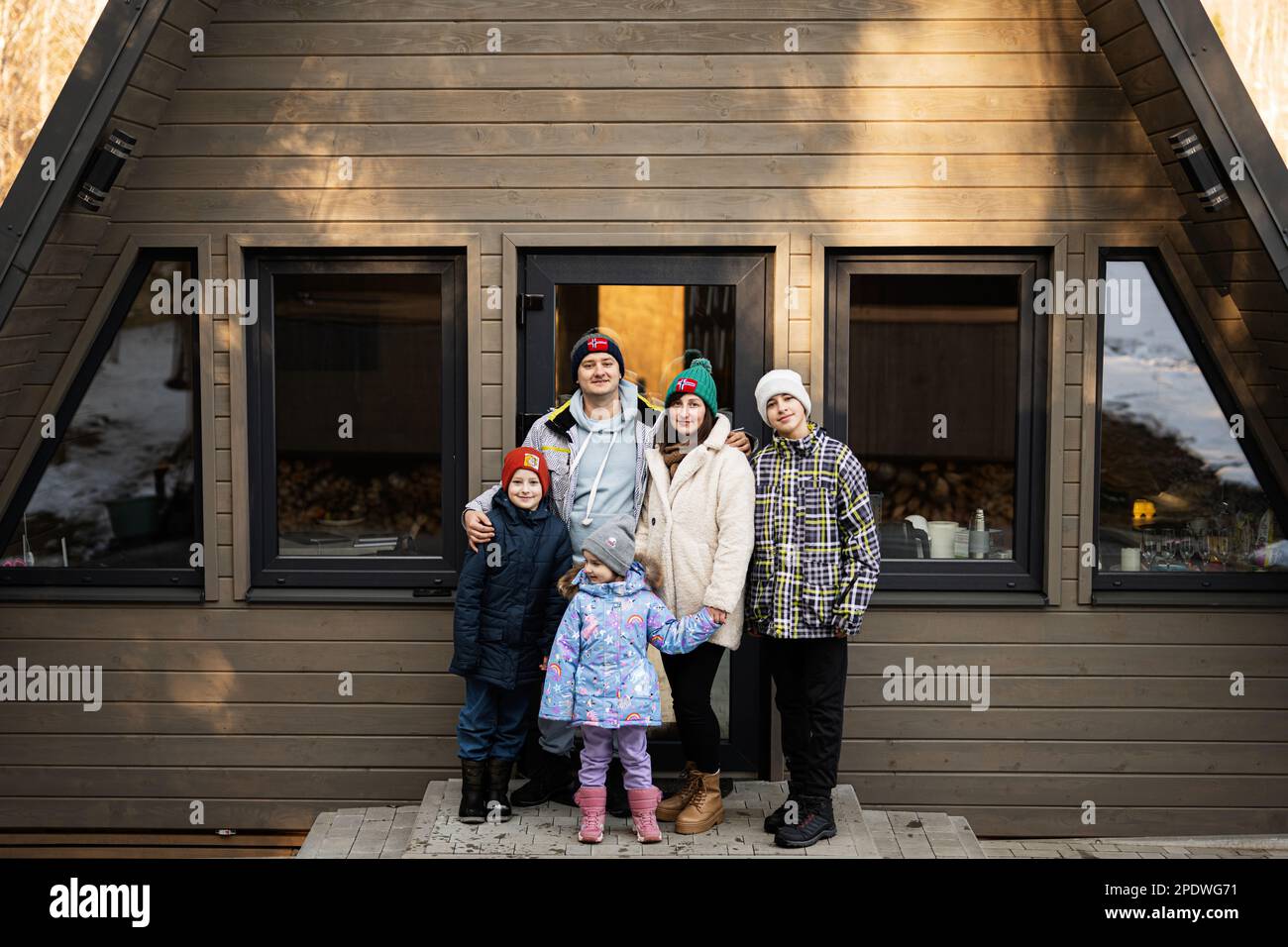 Famille avec trois enfants contre une petite maison de cabine en bois. Enfants à la campagne. Banque D'Images