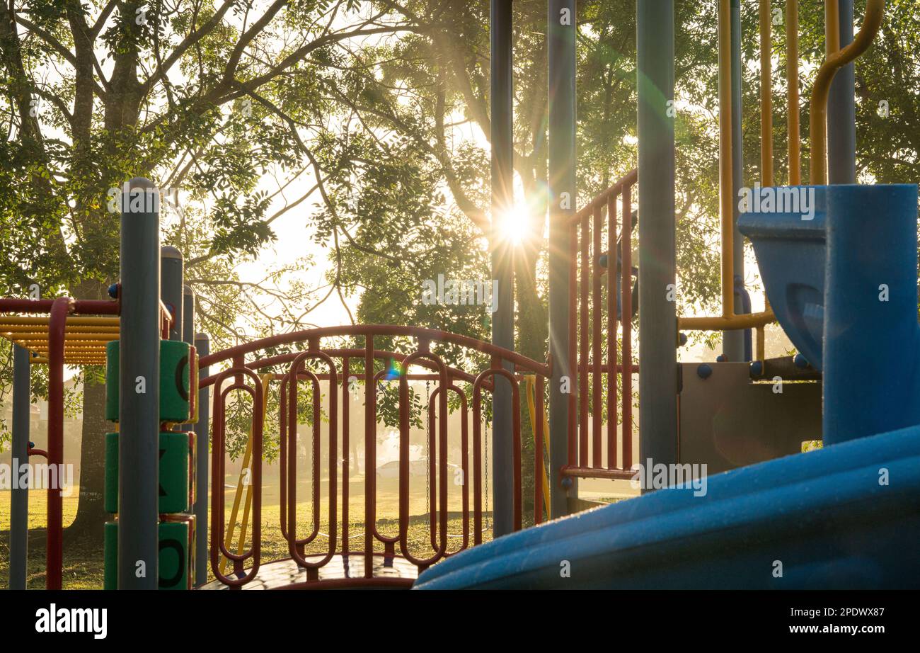 Aire de jeux colorée pour enfants dans un parc public avec des rayons du soleil le matin à l'arrière-plan. Banque D'Images