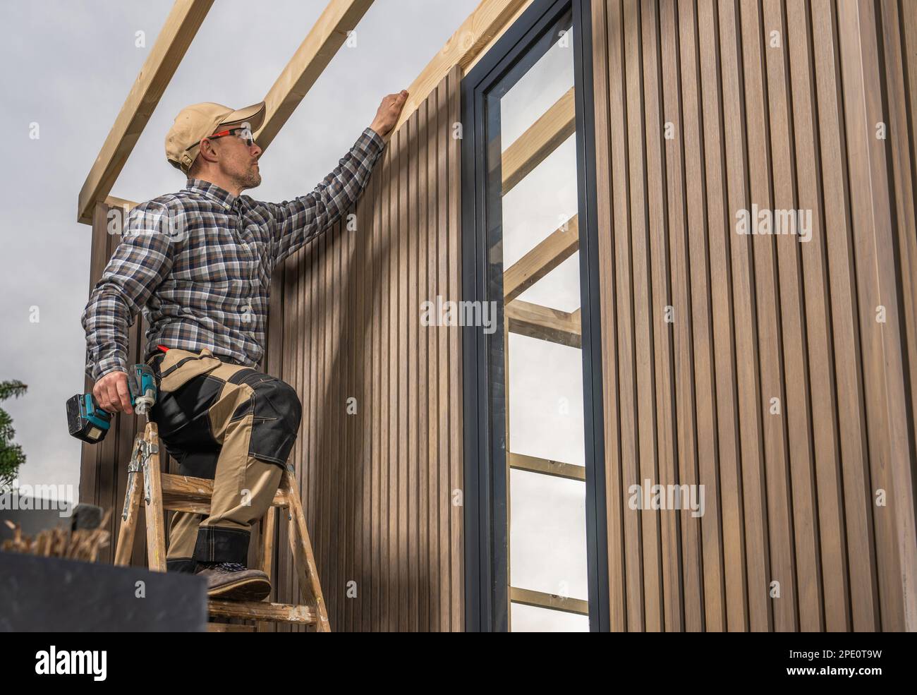 Ouvrier du bois caucasien expérimenté avec conducteur de perceuse sans fil dans ses mains construire jardin moderne Shed. Plaques de matériau composite. Banque D'Images