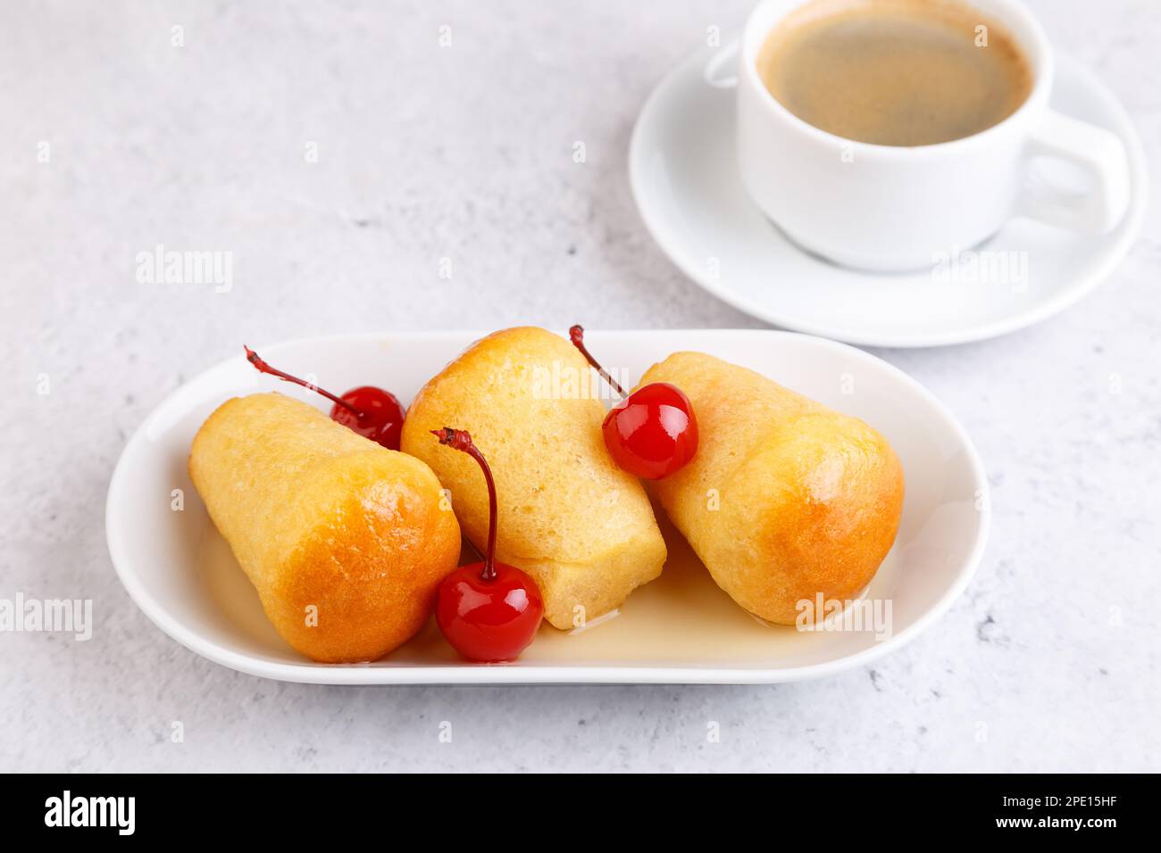 Rum baba napolitaine (ou baba au rhum) sur une assiette blanche avec un cocktail de cerise et une tasse de café. Petits gâteaux de levure trempés dans du sirop de rhum. Banque D'Images