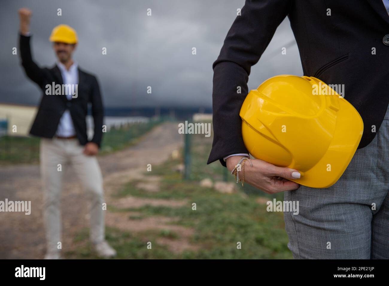 Un ingénieur tient un casque dans une main tandis que son collègue célèbre un succès au travail. Banque D'Images