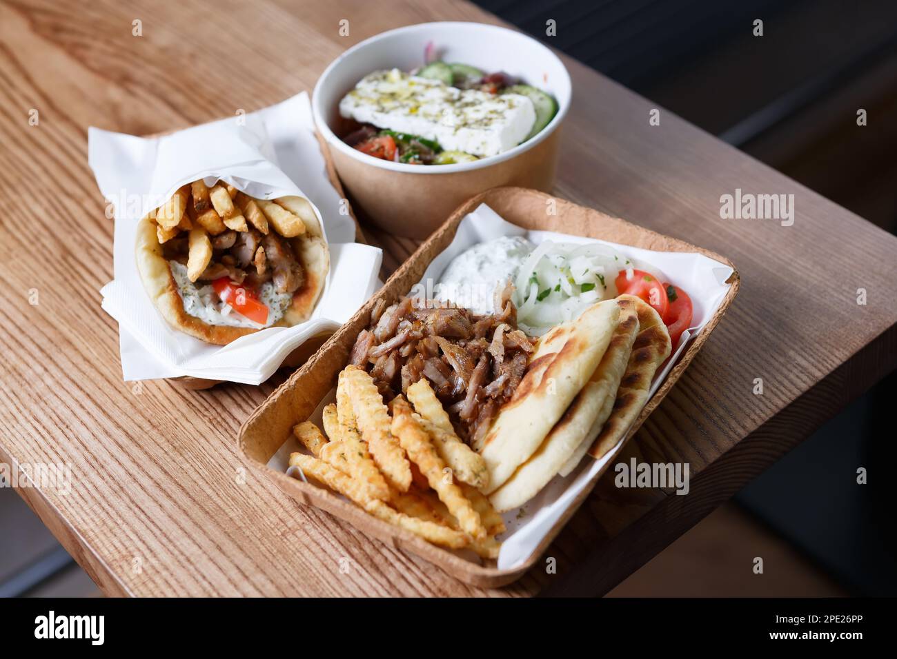 Restauration rapide grecque servie à emporter. Traditionnel pita souvlaki, gyros, salade grecque et pita avec frites servis dans une vaisselle en papier recyclable sur table. Banque D'Images