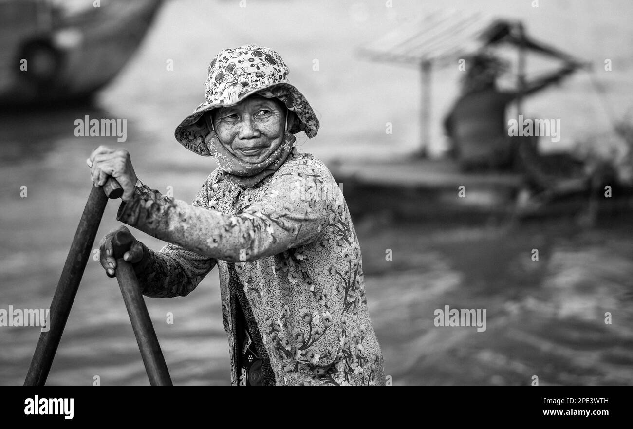 Une femme âgée se tient pour lamer son bateau sur le Mékong à long Xuyen dans le delta du Mékong au Vietnam. Banque D'Images