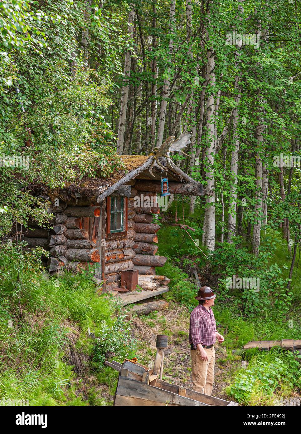 Fox, Alaska, Etats-Unis - 26 juillet 2011 : musée et parc de la mine d'or d'Eldorado. Le mineur se tient devant une cabane en bois située dans une forêt verte. Les bois d'orignal comme décora Banque D'Images