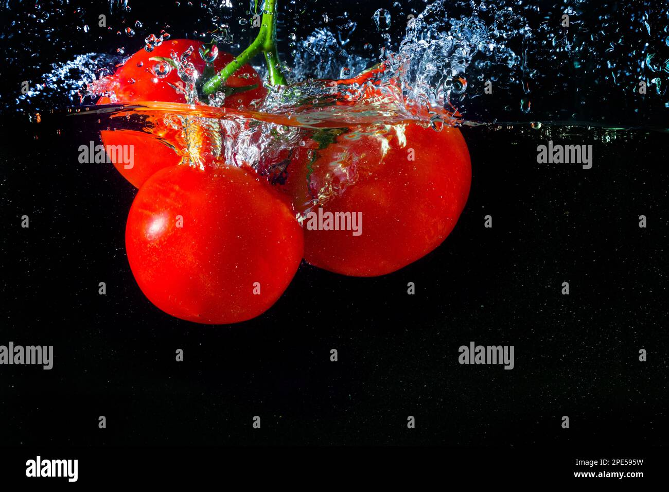 Tomate rouge fraîche tombant dans l'eau avec des éclaboussures d'eau et des bulles d'air isolées sur fond noir. Banque D'Images