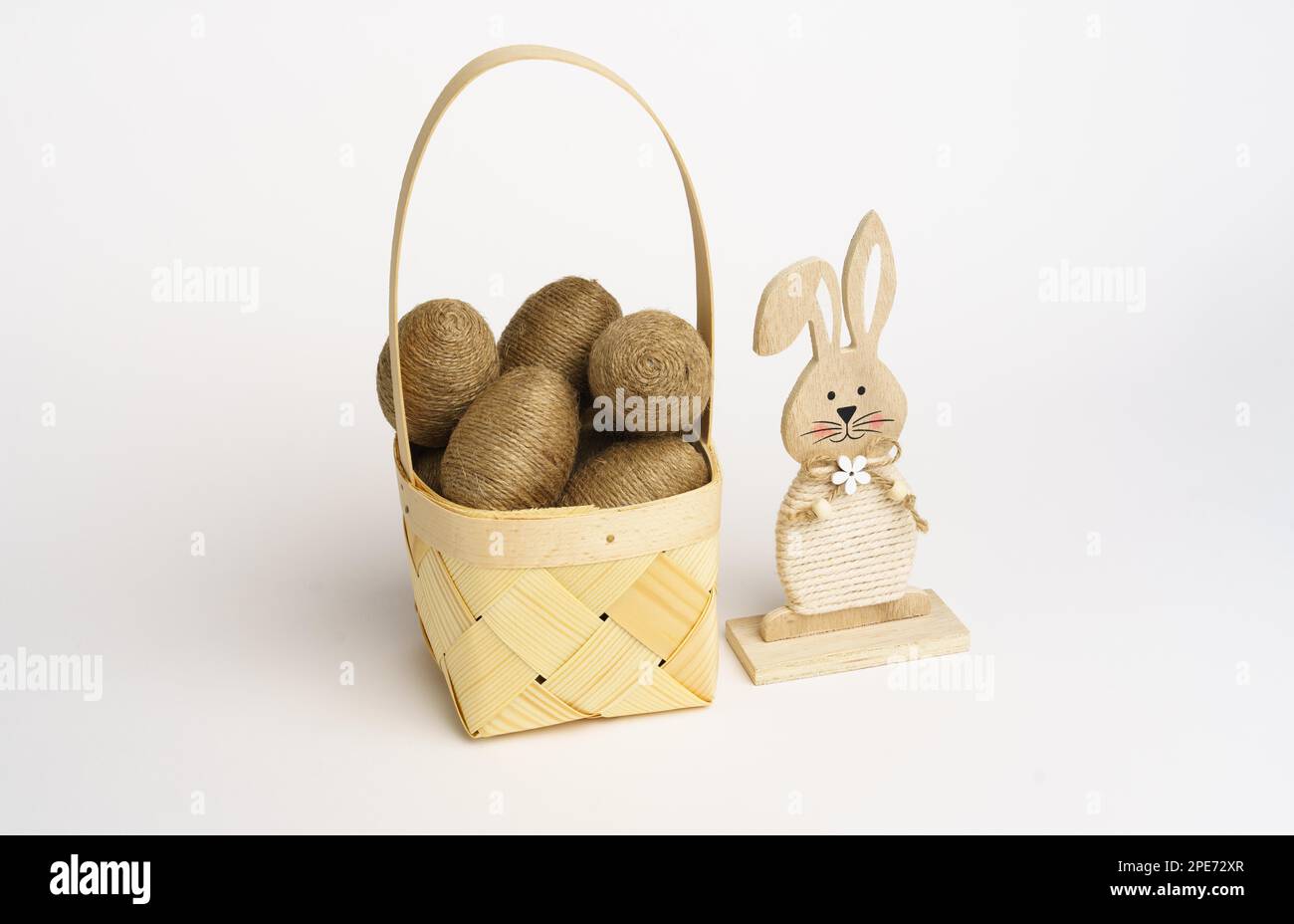 Composition de Pâques. Panier avec œufs enveloppés dans une ficelle de jute. Lapin en bois sur le côté. Arrière-plan blanc. Studio Banque D'Images