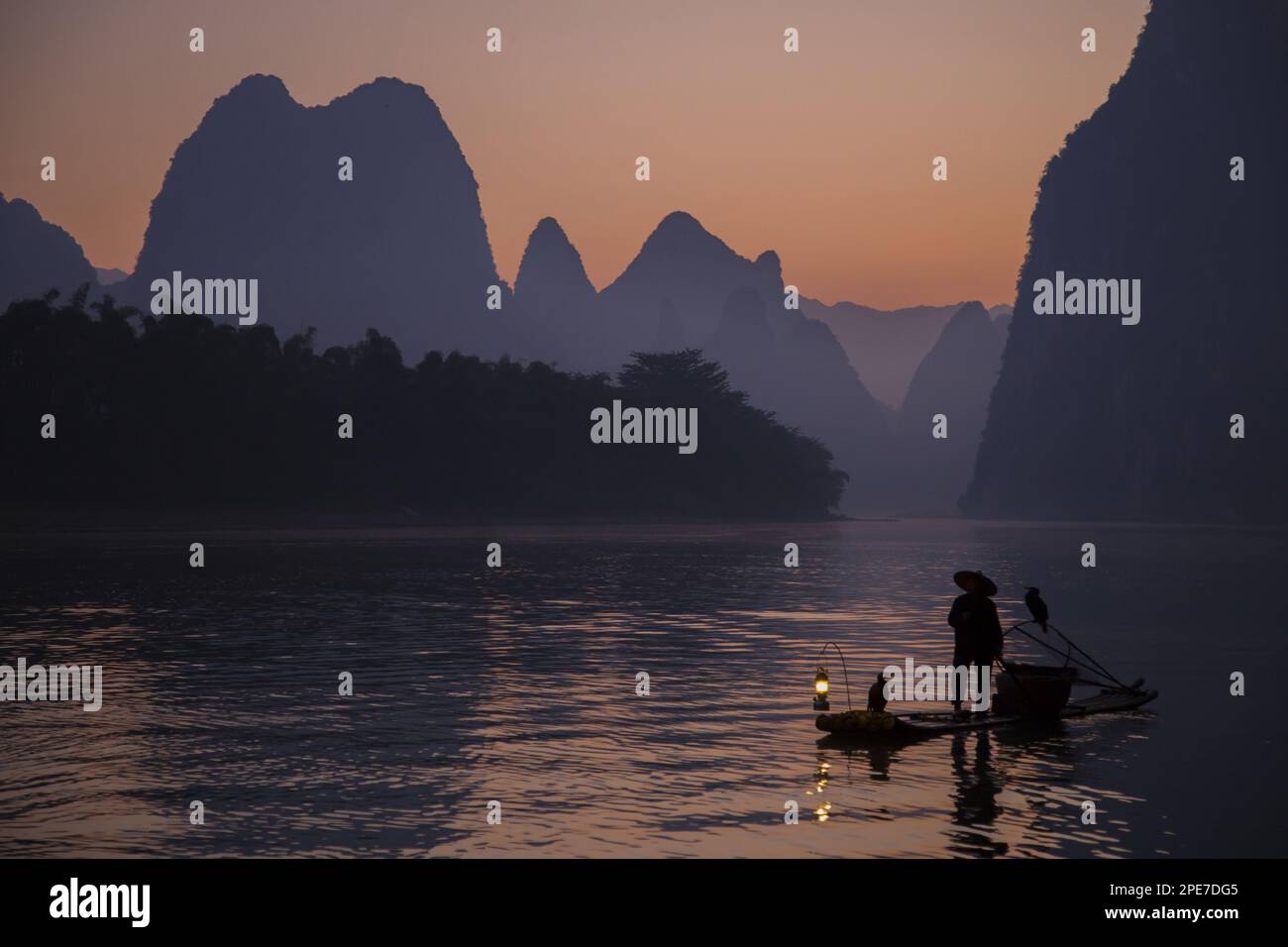 Pêcheur traditionnel avec cormorans entraînés debout sur un radeau de bambou au lever du soleil sur une rivière dans le secteur karst, Li River, Guilin, Guangxi Zhuang Banque D'Images