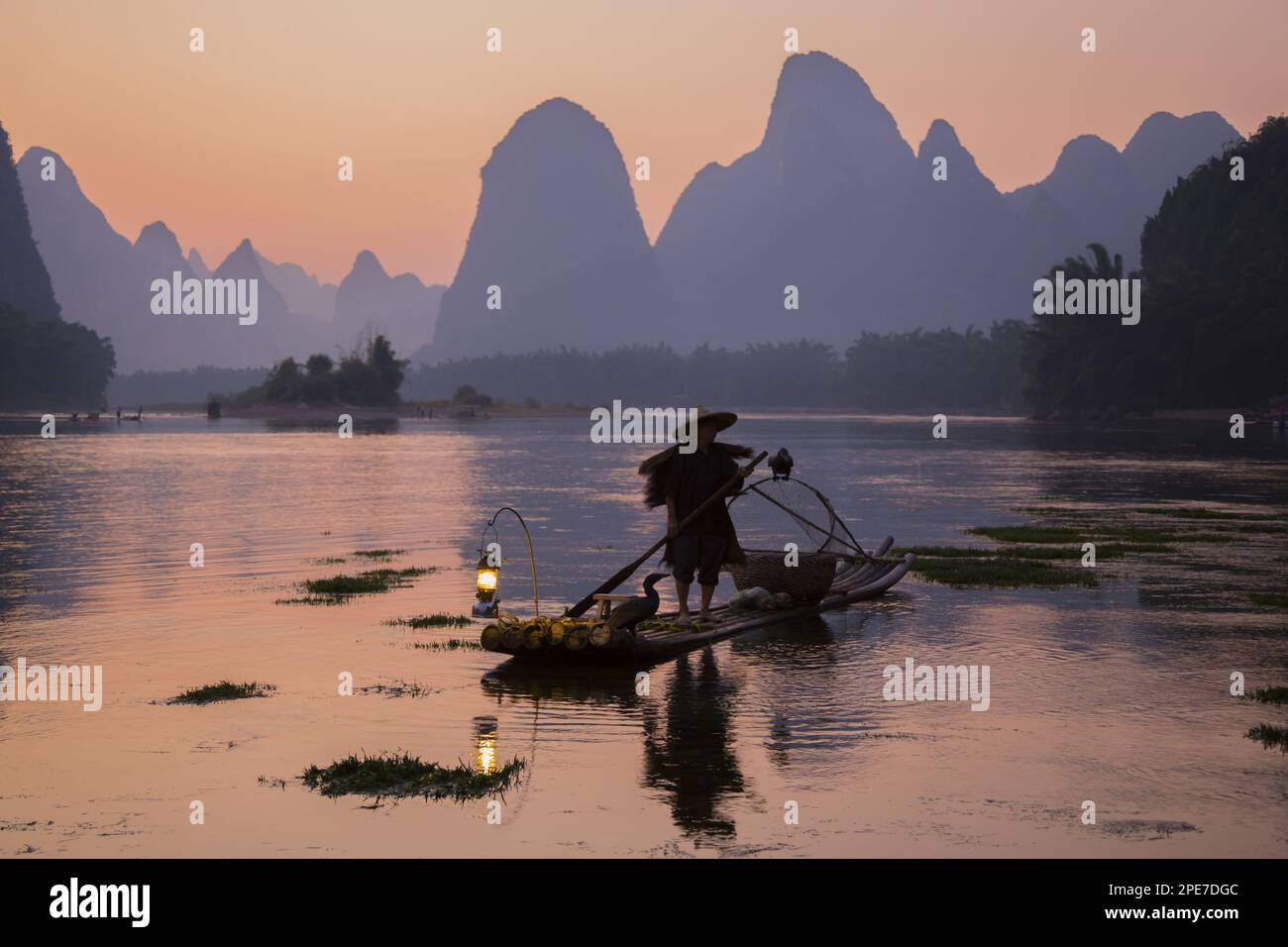 Pêcheur traditionnel avec cormorans entraînés debout sur un radeau de bambou au lever du soleil sur une rivière dans le secteur karst, Li River, Guilin, Guangxi Zhuang Banque D'Images