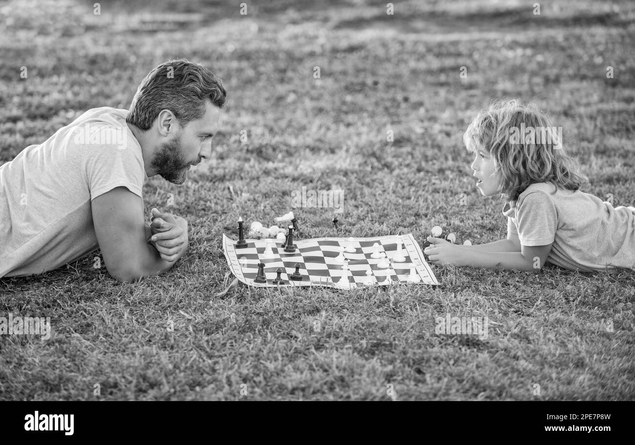 famille heureuse de parents et fils enfant jouant aux échecs sur l'herbe verte dans le parc extérieur, jeu d'échecs Banque D'Images