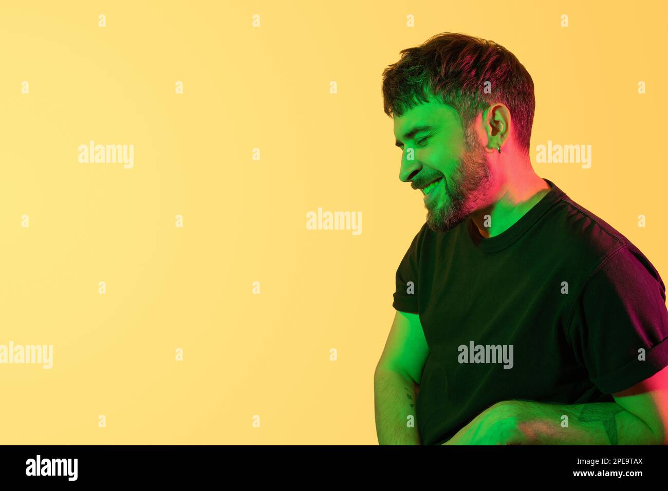 Portrait créatif. Homme souriant avec les yeux fermés en vert, lumières néon rose sur fond jaune. Photo moderne beau barbu homme d'âge moyen Banque D'Images