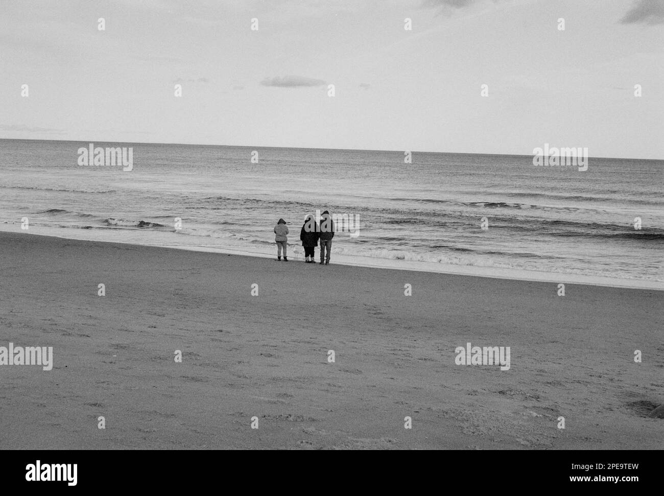 Trois visiteurs se tiennent sur le rivage pour observer la marée et les vagues à Salisbury Beach, Massachusetts. L'image a été capturée en noir et blanc analogique Banque D'Images