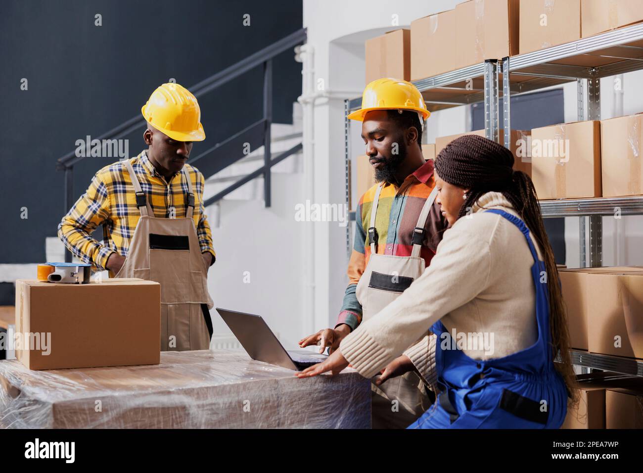 Les gestionnaires de colis afro-américains emballant des colis et vérifiant la liste des commandes sur ordinateur portable. Tous les travailleurs d'entrepôt noirs, hommes et femmes, s'intéressent au ticket de ramassage électronique dans la salle de stockage Banque D'Images