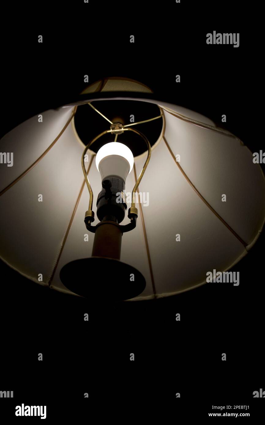 En regardant à l'intérieur d'une lampe avec une nouvelle lumière LED qui illumine une pièce sombre. Support de lampe en laiton avec abat-jour illustré. Banque D'Images