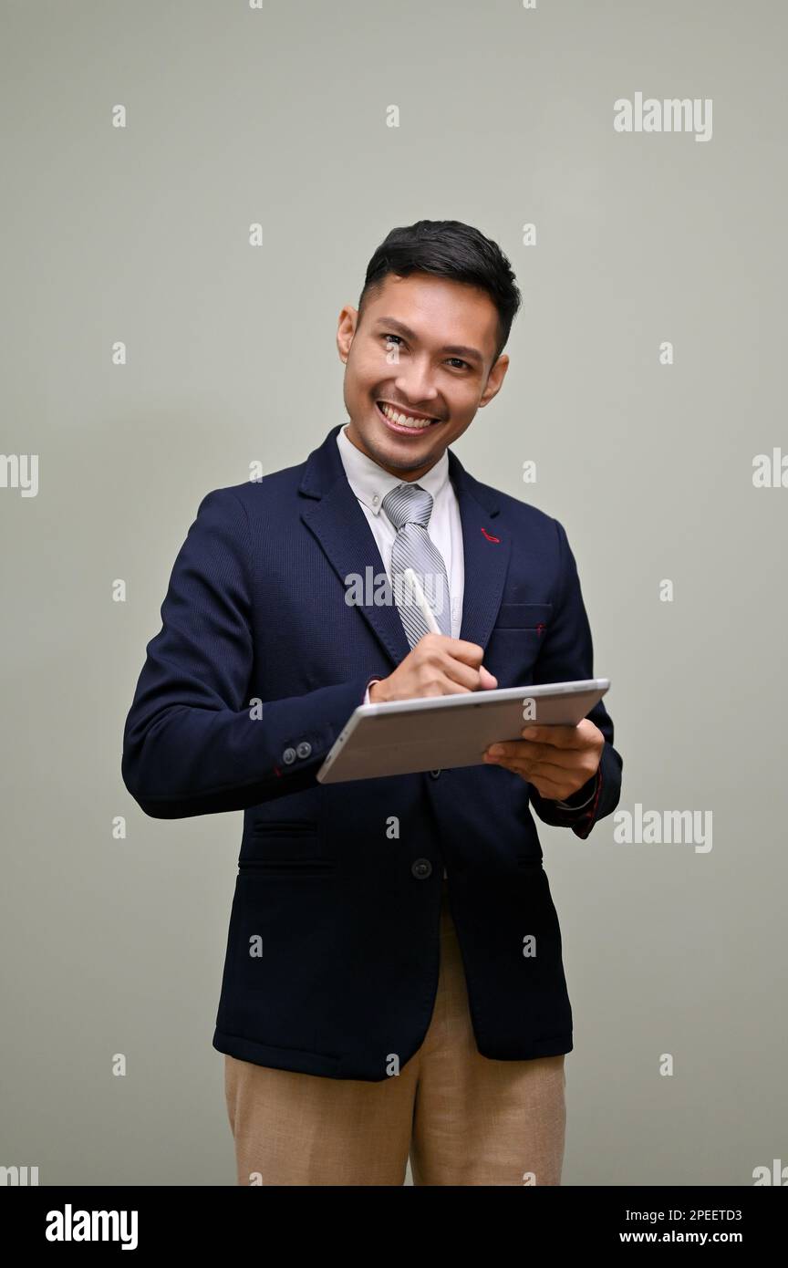 Portrait, souriant et heureux hommes d'affaires asiatiques du millénaire en costume formel à l'aide de sa tablette numérique et regardant l'appareil photo tout en étant debout aga Banque D'Images