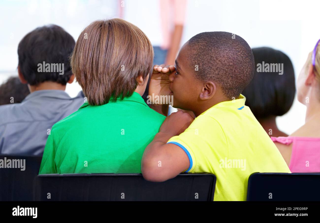 Je n'ai pas envie de travailler. Un jeune écolier chuchote dans l'oreille de ses amis pendant la classe. Banque D'Images