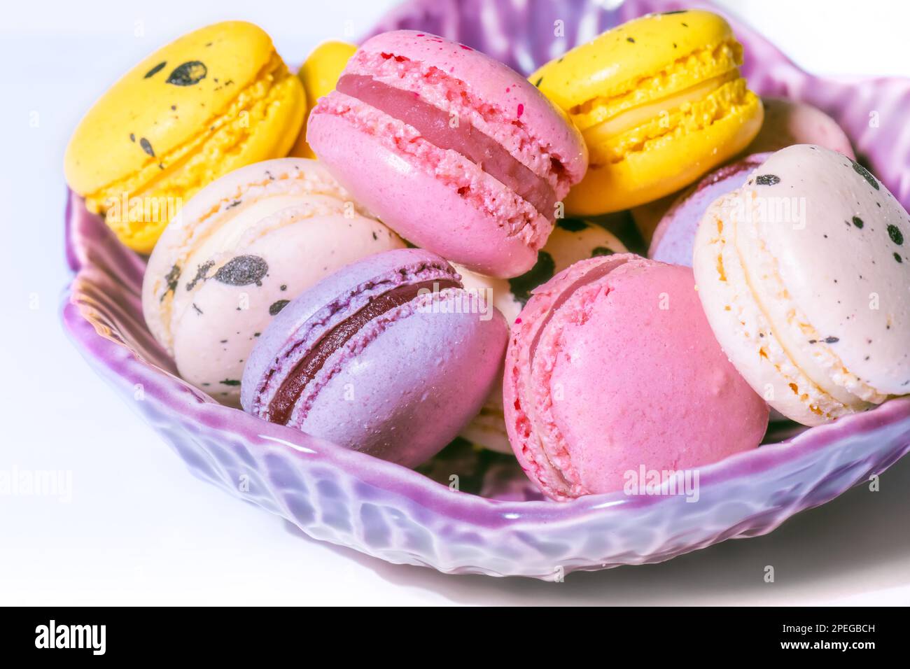 Macarons doux macarons dans un bol sur fond blanc. Petits gâteaux français à la vanille, à la framboise, au citron et à la fraise. Carte de pâtisserie Banque D'Images