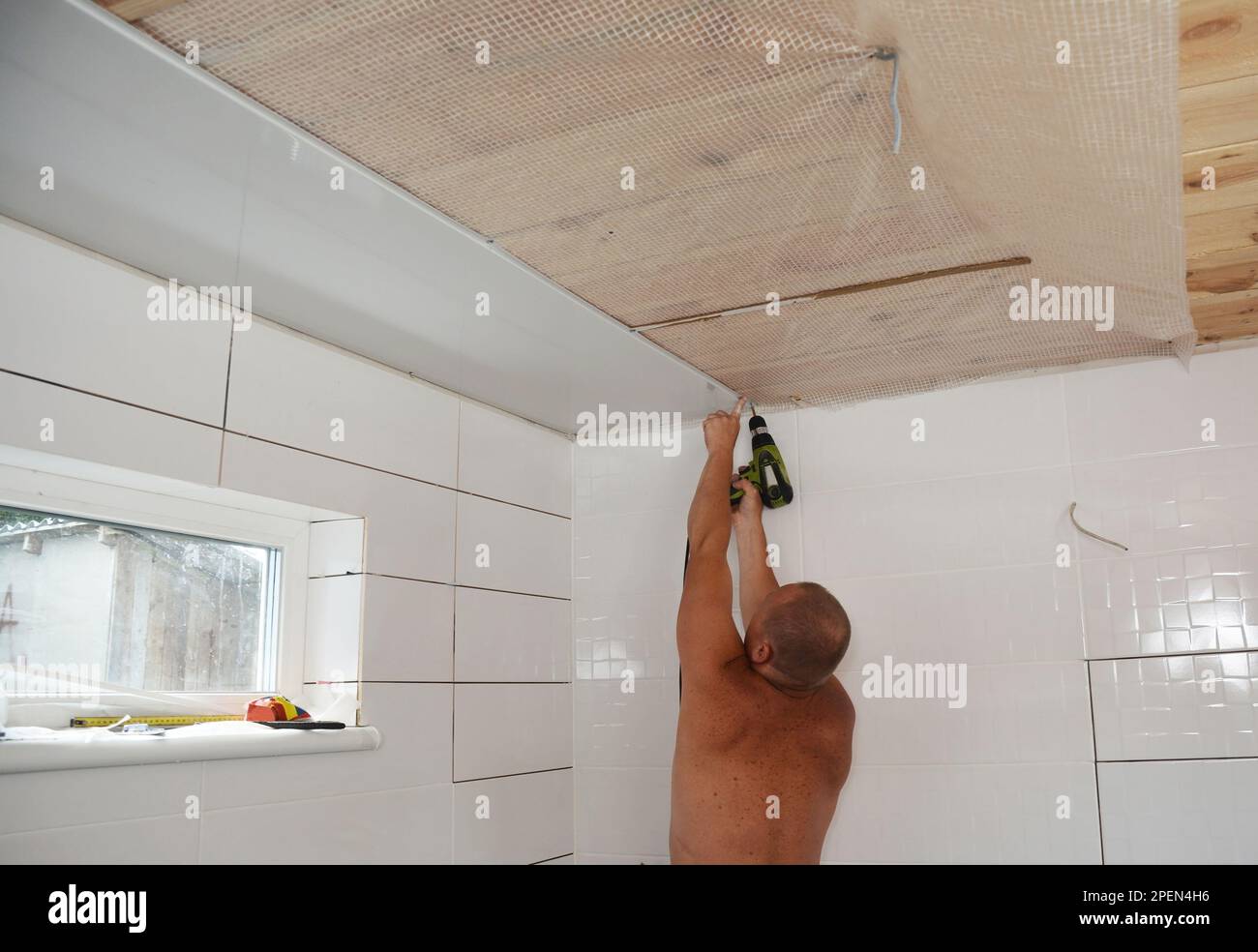 Entrepreneur installant des panneaux de plafond en PVC blanc avec pistolet à vis dans la salle de bains de la nouvelle maison. Installation de panneaux de plafond en PVC. Banque D'Images