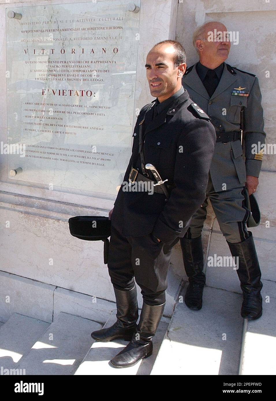 Dressed with the uniform of an Italian Fascist military officer,  professional extra Sergio Albanesi, background, and an unidentified "camicie  nere" (black shirts) colleague, look on next a dress-code and regulations  sign, while
