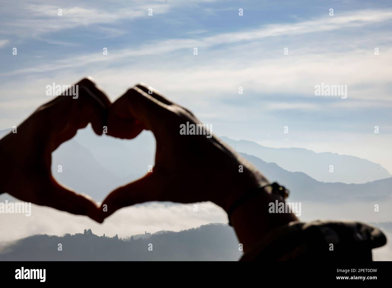 Femme faisant une forme de coeur avec ses mains avec Mountain Range au-dessus de Cloudscape lors d'une Journée de soleil à Lugano, Tessin en Suisse. Banque D'Images