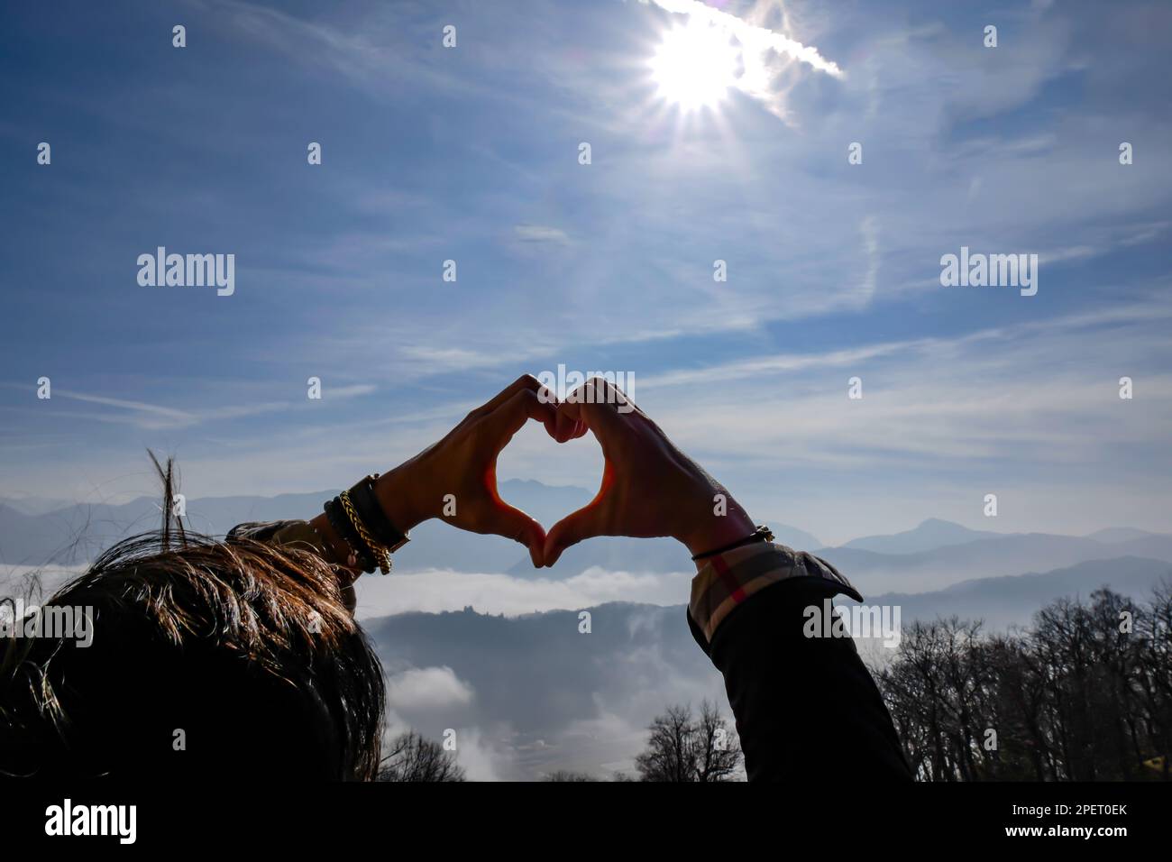 Femme faisant une forme de coeur avec ses mains avec Mountain Range au-dessus de Cloudscape lors d'une Journée de soleil à Lugano, Tessin en Suisse. Banque D'Images