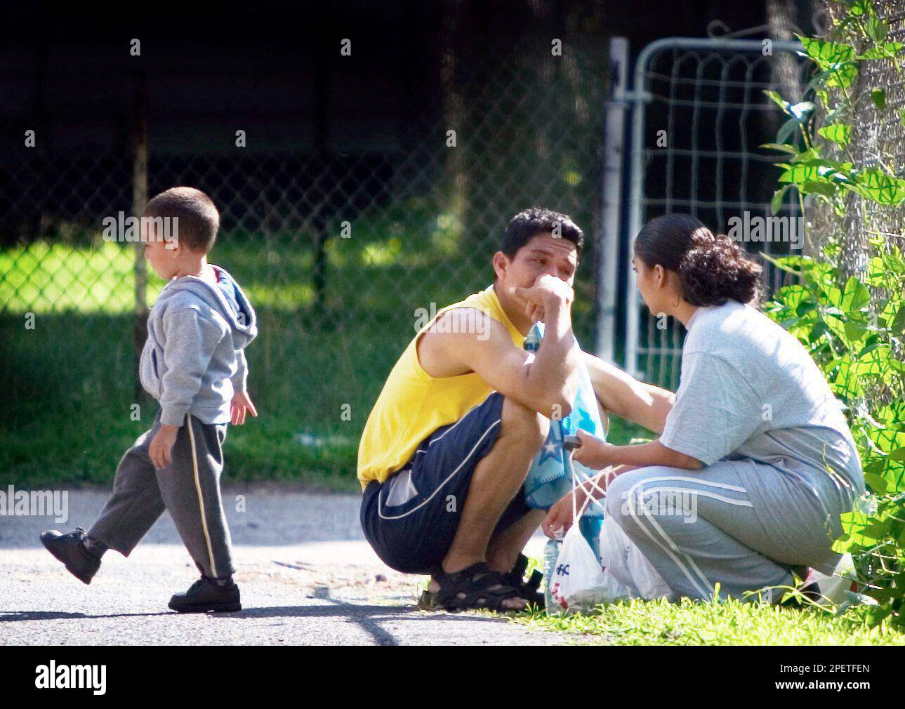 Eddy Carias, 2, occupies himself at left while his dad Edin Carias, center, and mother Sury Chilin, right, console one another after an early morning fire in Trenton, N.J. claimed the lives of three people Monday, July 26, 2004. Carias and Chilin lived next door to the fire. Investigators are trying to determine what caused a fire that killed a woman and her two young sons in Trenton this morning. (AP Photo/NJ Advance Media, Michael Mancuso) Banque D'Images