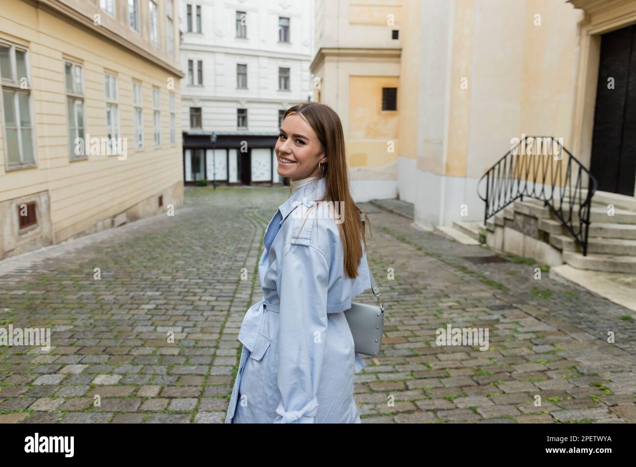 Jeune femme gaie dans un manteau de tranchée bleu marchant près des  bâtiments de la rue à Vienne Photo Stock - Alamy