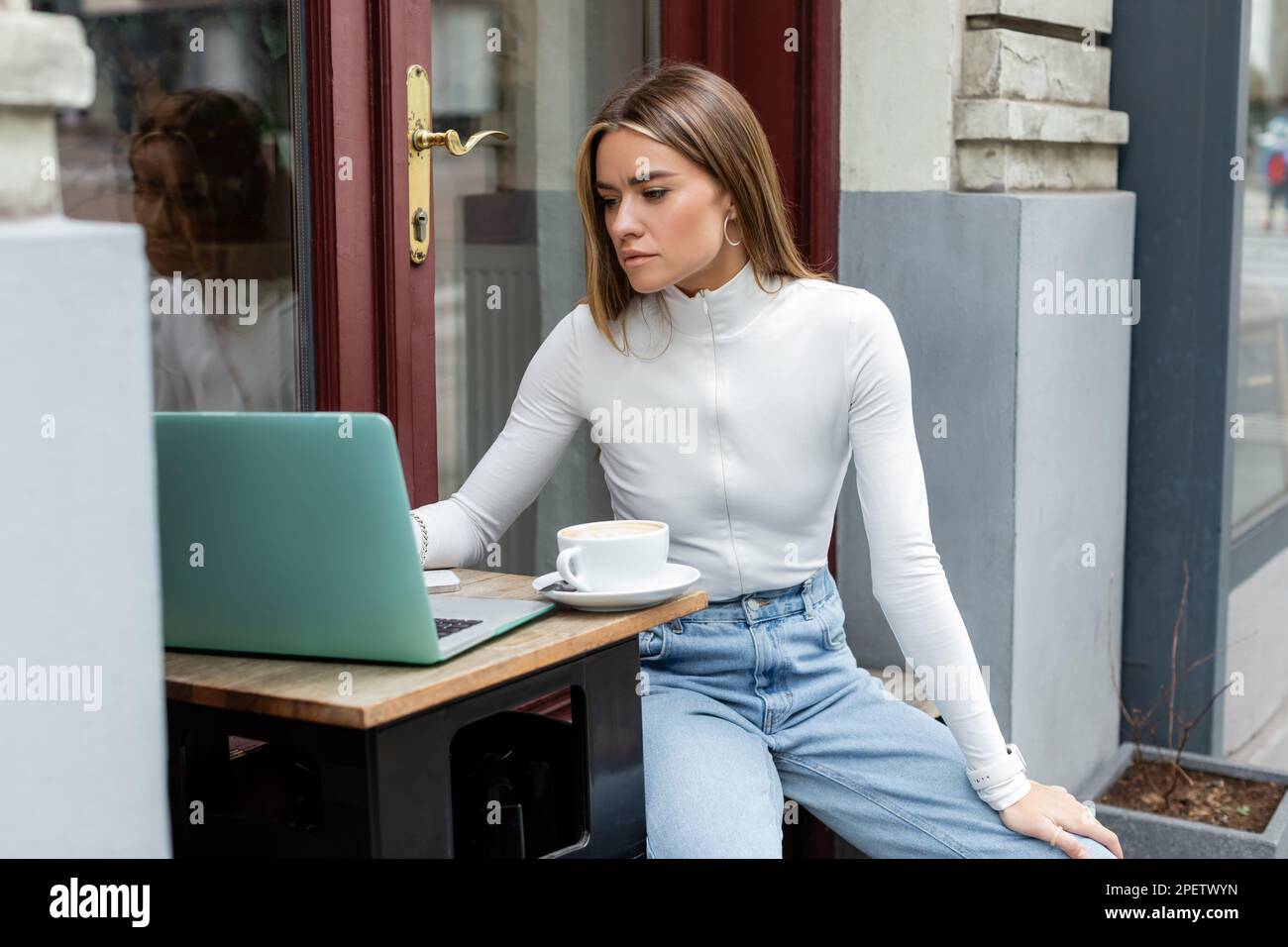 Jeune femme utilisant un ordinateur portable près d'une tasse de café tout en étant assise dans un café à l'extérieur à Vienne Banque D'Images