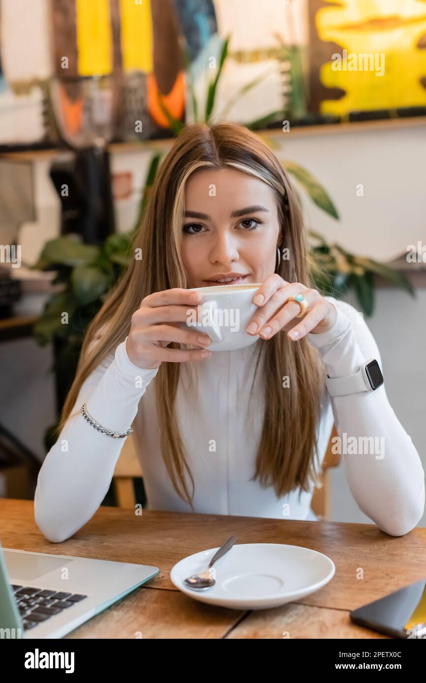 Une jeune femme boit du cappuccino près d'un ordinateur portable sur une table dans un café de Vienne Banque D'Images