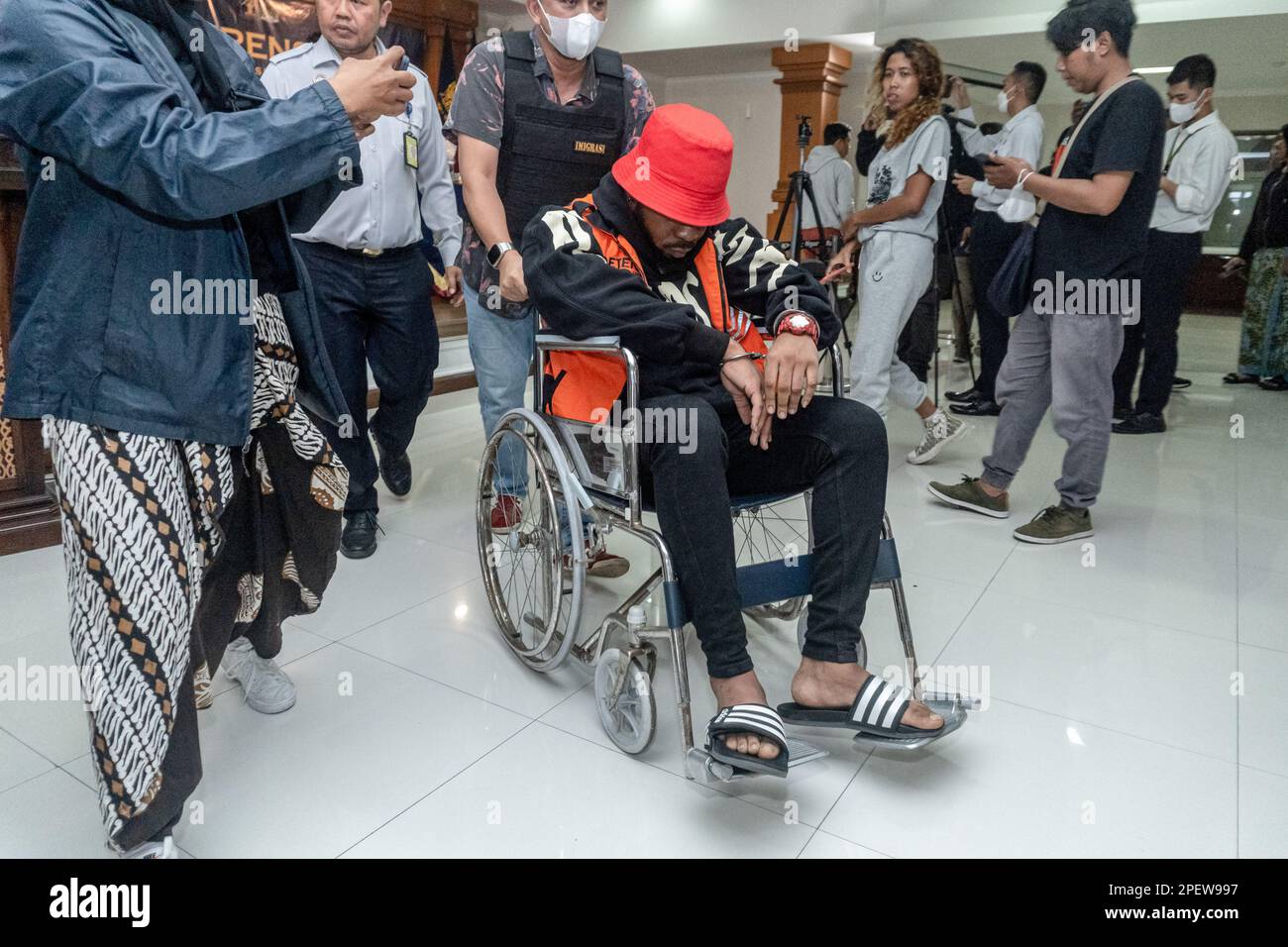 Un agent d'immigration escorte un détenu national nigérian, qui est assis en fauteuil roulant alors qu'il tombe malade pendant la conférence de presse d'expulsion. Les autorités de Bali ont expulsé deux ressortissants britanniques et deux ressortissants nigérians pour surséjour. Le gouverneur de Bali, I Wayan Koster, a annoncé dimanche, 12 mars 2023, Que la politique de visa à l'arrivée (VoA) pour les ressortissants ukrainiens et russes sera révoquée afin de réduire les violations du tourisme, qui sont principalement commises par ces deux nationalités. En 2022, la province de Bali a expulsé 194 étrangers, la majorité pour séjour excessif et travail illégal. Banque D'Images