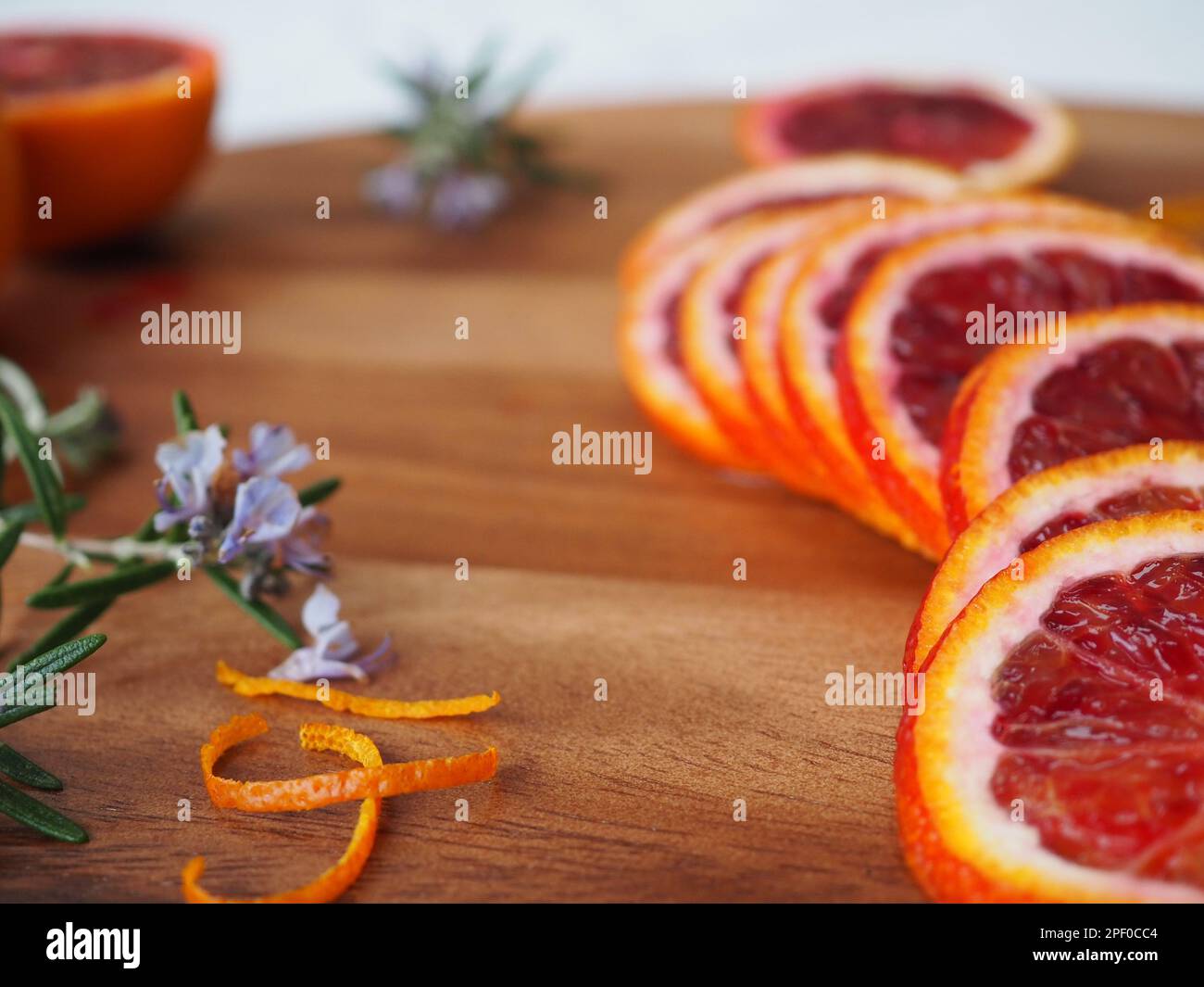 Gros plan d'oranges fraîchement tranchées (moro sicilien) sur une planche à découper avec des branches de romarin fleuri et des boucles de zeste d'orange Banque D'Images
