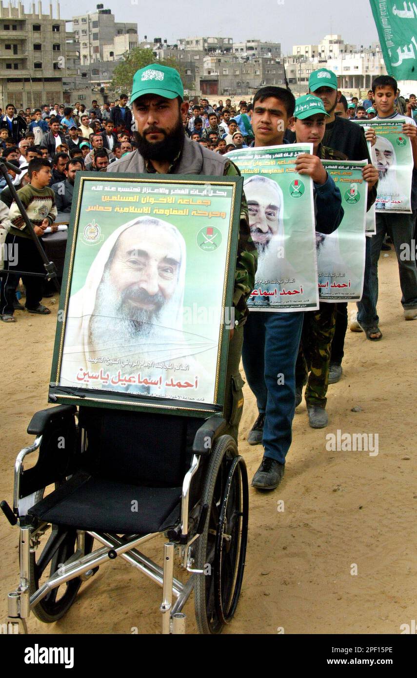 Palestinian Hamas supporters march behind a wheelchair decorated to represent former Hamas spiritual leader Sheikh Ahmed Yassin, in posters, who was killed last month in an Israeli airstrike in Gaza, during a rally and memorial service in the Jabaliya refugee camp southern Gaza Strip, Friday, April 2, 2004. (AP Photo/Adel Hana) Banque D'Images