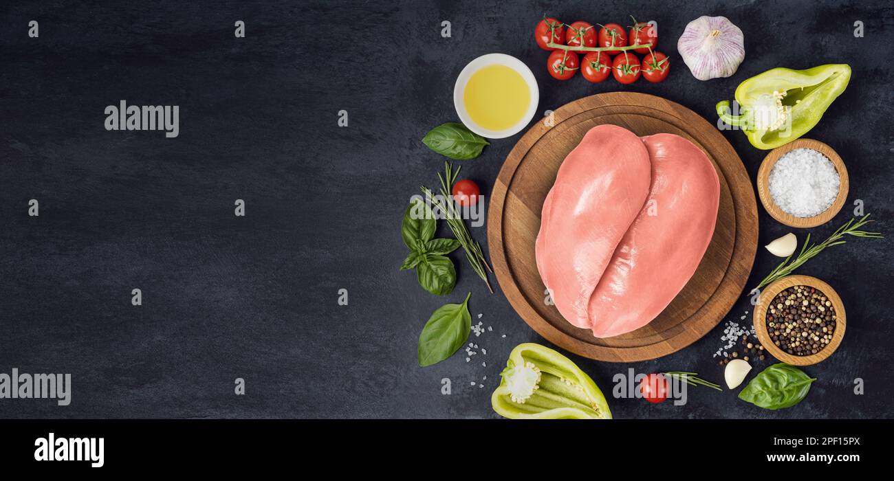 Filets de poulet crus sur planche à découper en bois et épices, herbes pour nourriture sur table en pierre noire. Vue de dessus Banque D'Images
