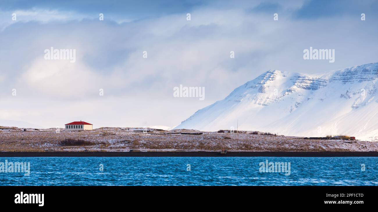 Paysage islandais côtier avec maison résidentielle et montagnes enneigées sous ciel nuageux. Reykjavik, Islande Banque D'Images