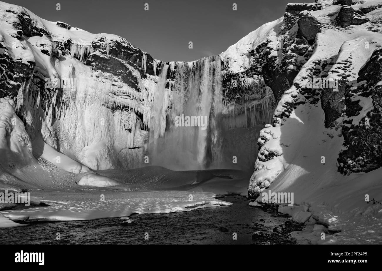 Cascade Skógafoss géante entièrement couverte de neige et la rivière passe à côté. Le soleil de l'aube illumine l'eau qui tombe de l'aquarelle Banque D'Images