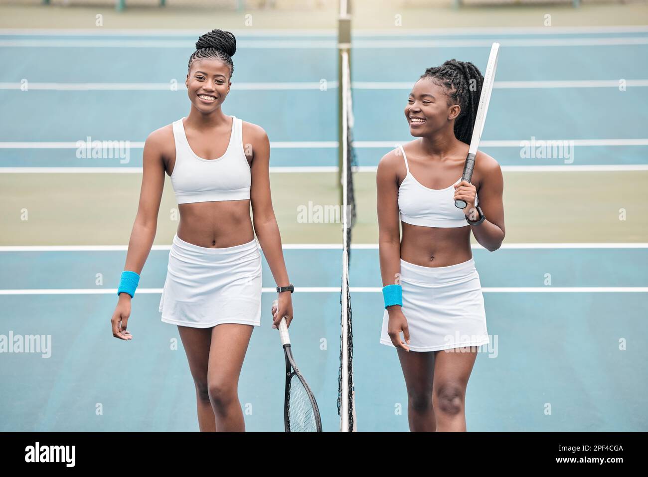 jeunes filles insouciantes qui parlent après un match de tennis. Deux athlètes professionnels tenant leurs raquettes de tennis sur le court. Jeunes femmes marchant sur le filet Banque D'Images