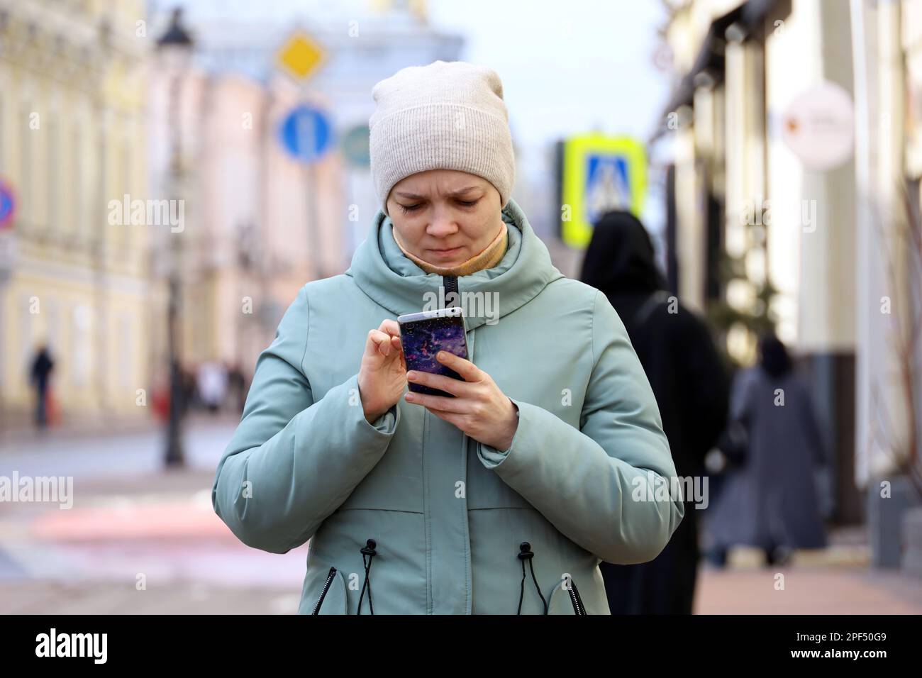 Femme portant un manteau et un chapeau lisant un smartphone dans la rue. Utilisation d'un téléphone portable au printemps Banque D'Images