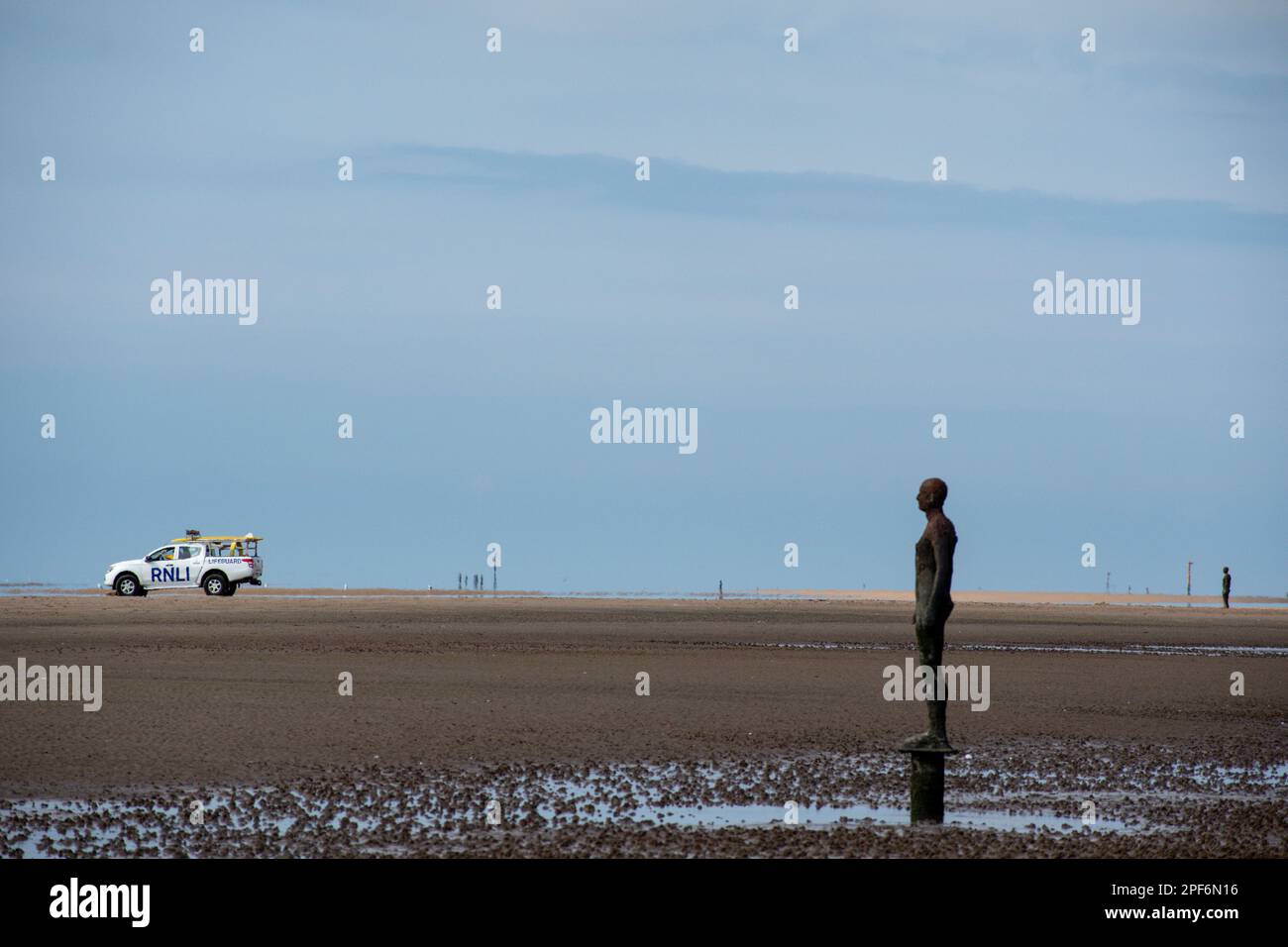 Figure de l'installation de l'artiste Antony Gormley un autre endroit sur Crosby Beach face à la mer avec un RNLI LIFE Guard 4x4 en arrière-plan Banque D'Images