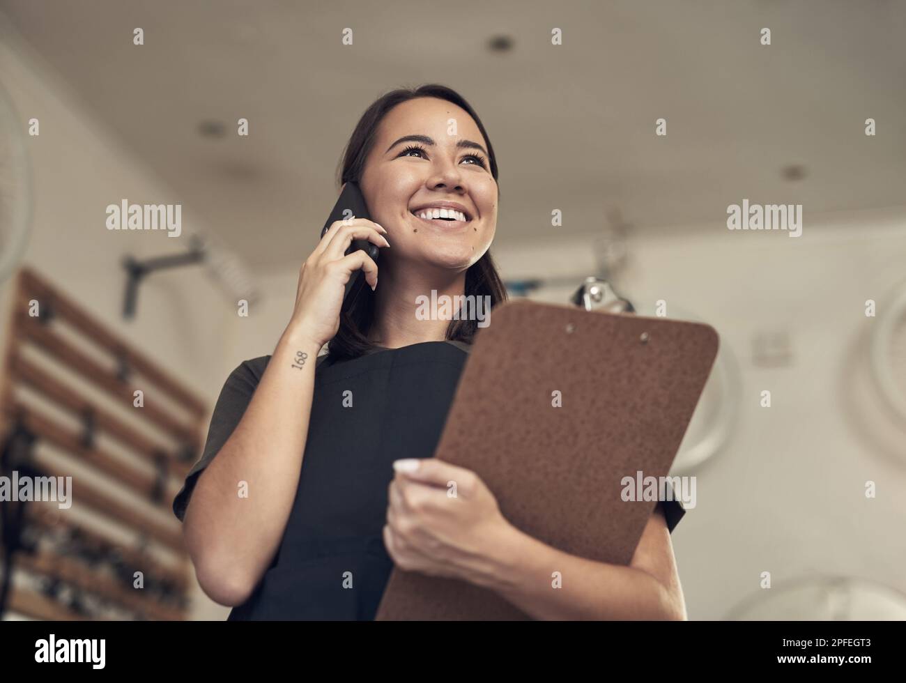Voulez-vous que je vous expédie votre vélo ? une jeune femme attrayante debout seule dans son magasin de vélos et utilisant son téléphone portable tout en tenant un Banque D'Images