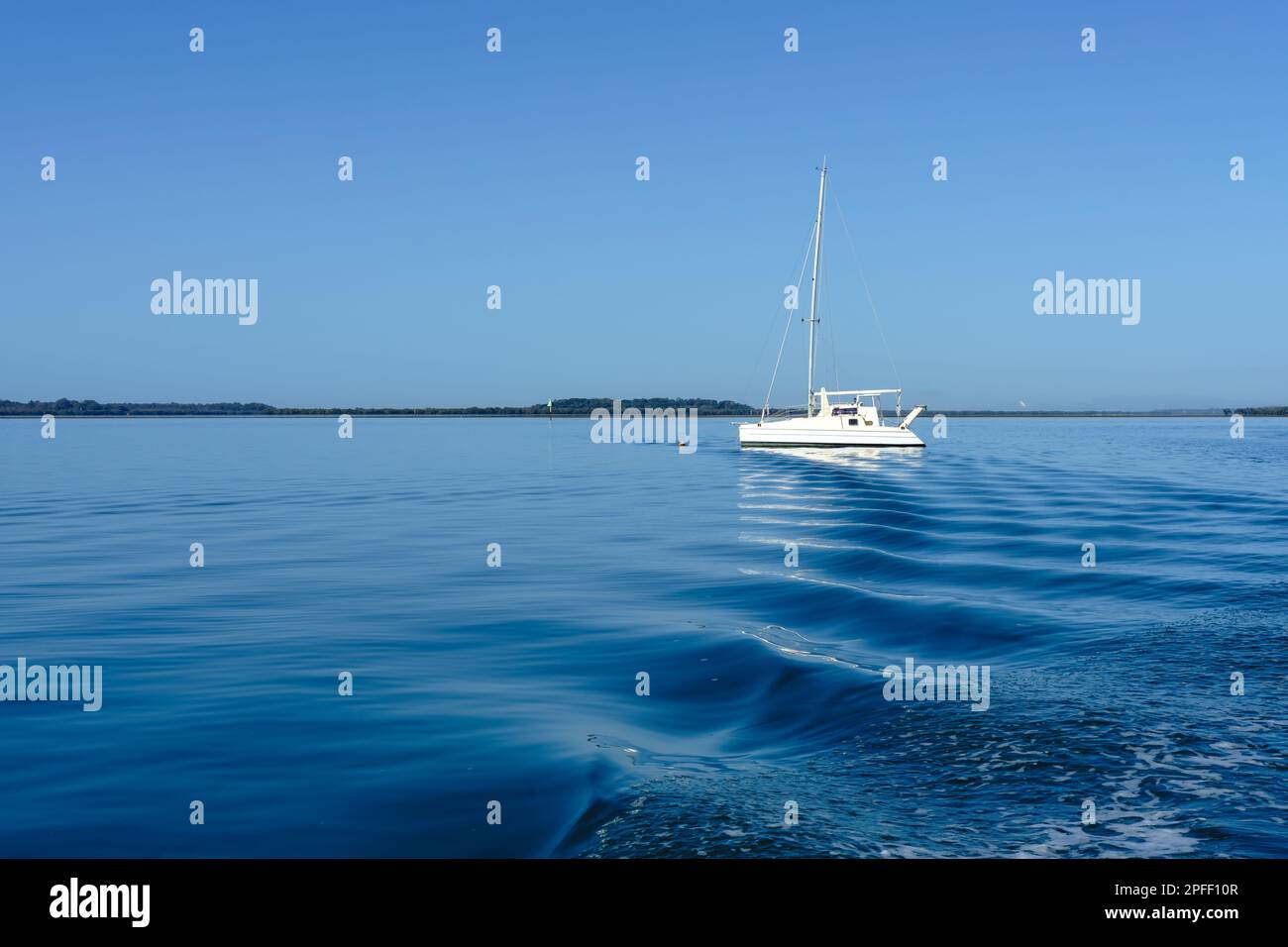 Les ondulations de la station de lavage derrière un bateau conduisent l'œil à un seul bateau blanc sur les eaux calmes et bleues au large de l'île de Coochiemudlo Banque D'Images