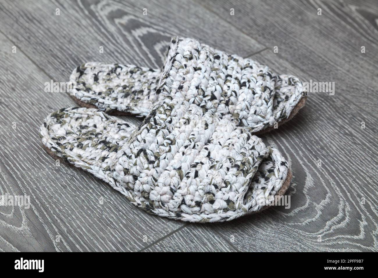 Des pantoufles faites à la main en tricot blanc se tiennent sur un parquet gris Banque D'Images
