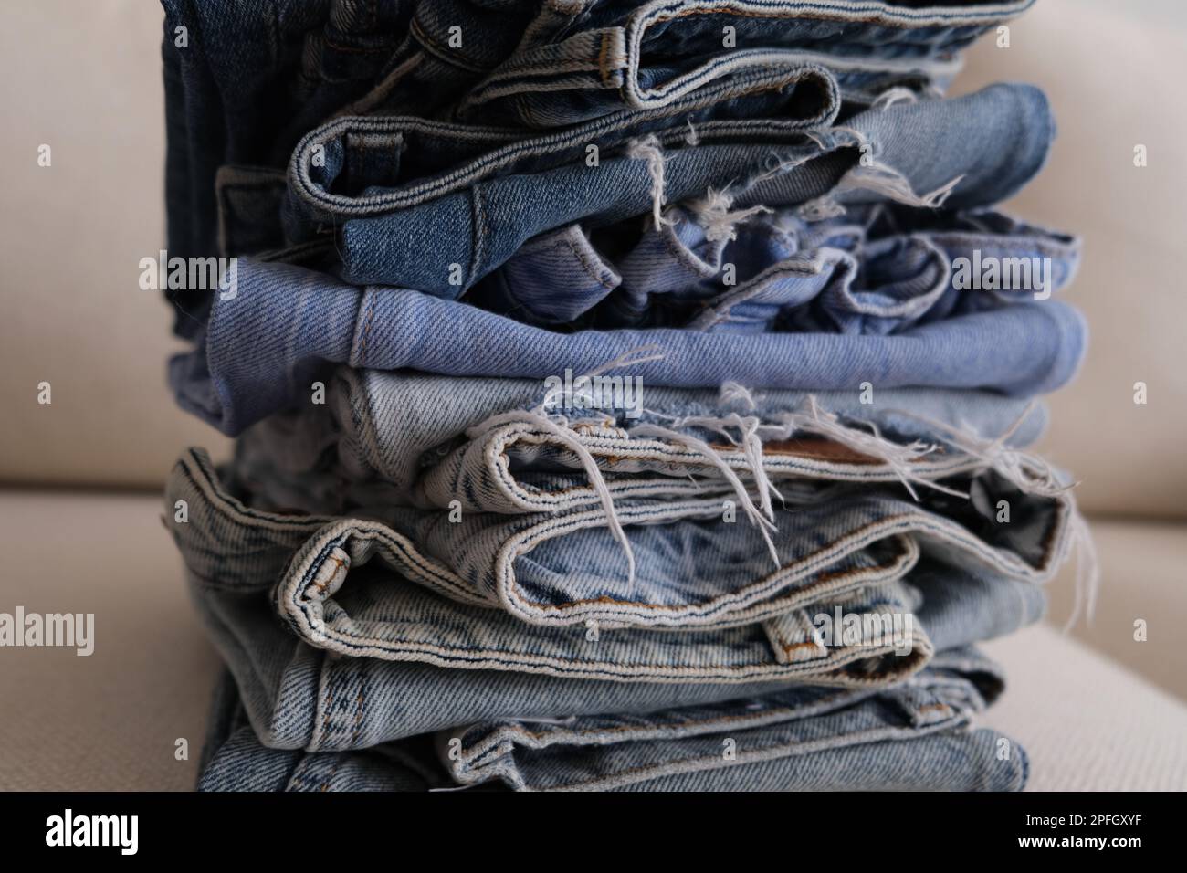 Pantalon denim organisé, pile de différentes nuances de jeans denim sur un canapé blanc. Pantalon en denim plié dans une rangée sur un fauteuil blanc. Banque D'Images