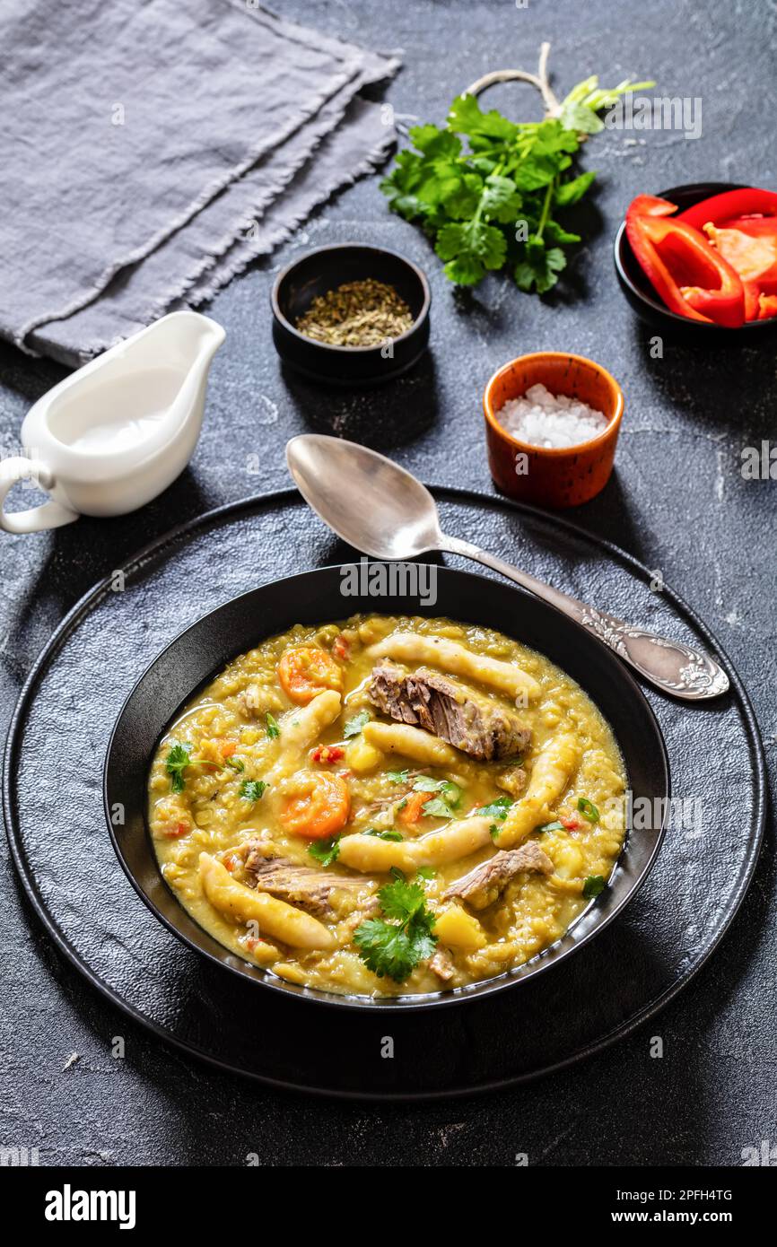 petits pois, soupe de petits pois avec boulettes et bœuf dans un bol noir sur table en béton avec ingrédients, cuisine jamaïcaine, vue verticale d'en haut, clo Banque D'Images