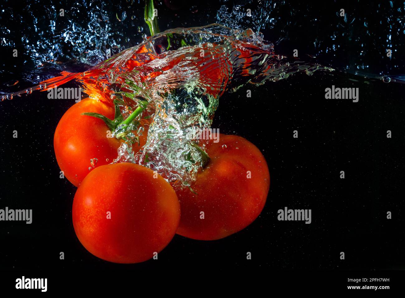 Tomate rouge fraîche tombant dans l'eau avec des éclaboussures d'eau et des bulles d'air isolées sur fond noir. Banque D'Images