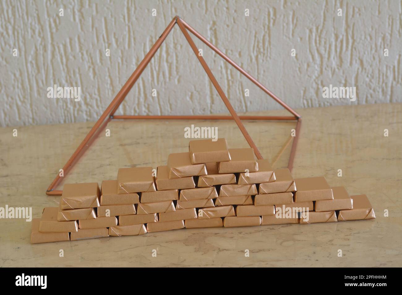 Chocolat. Barres de chocolat faites à la main enveloppées de papier doré en forme de pyramide sur une table en marbre travertitive avec pyramide de cuivre dans le fond, BR Banque D'Images