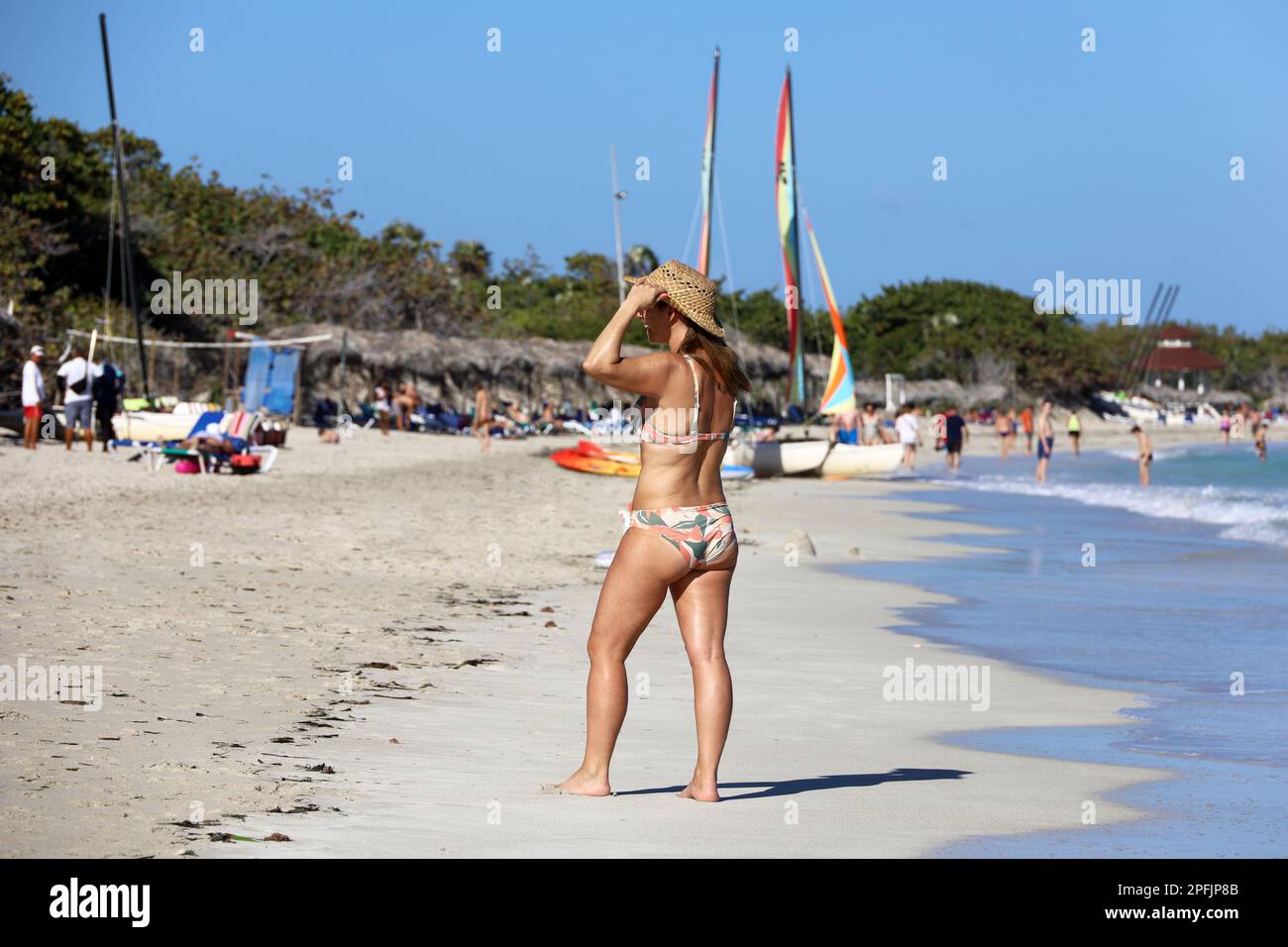 Bonne femme en bikini de bronzage sur la plage de sable tropical sur les voiliers et les gens de fond. Vacances sur la côte atlantique de l'océan Banque D'Images