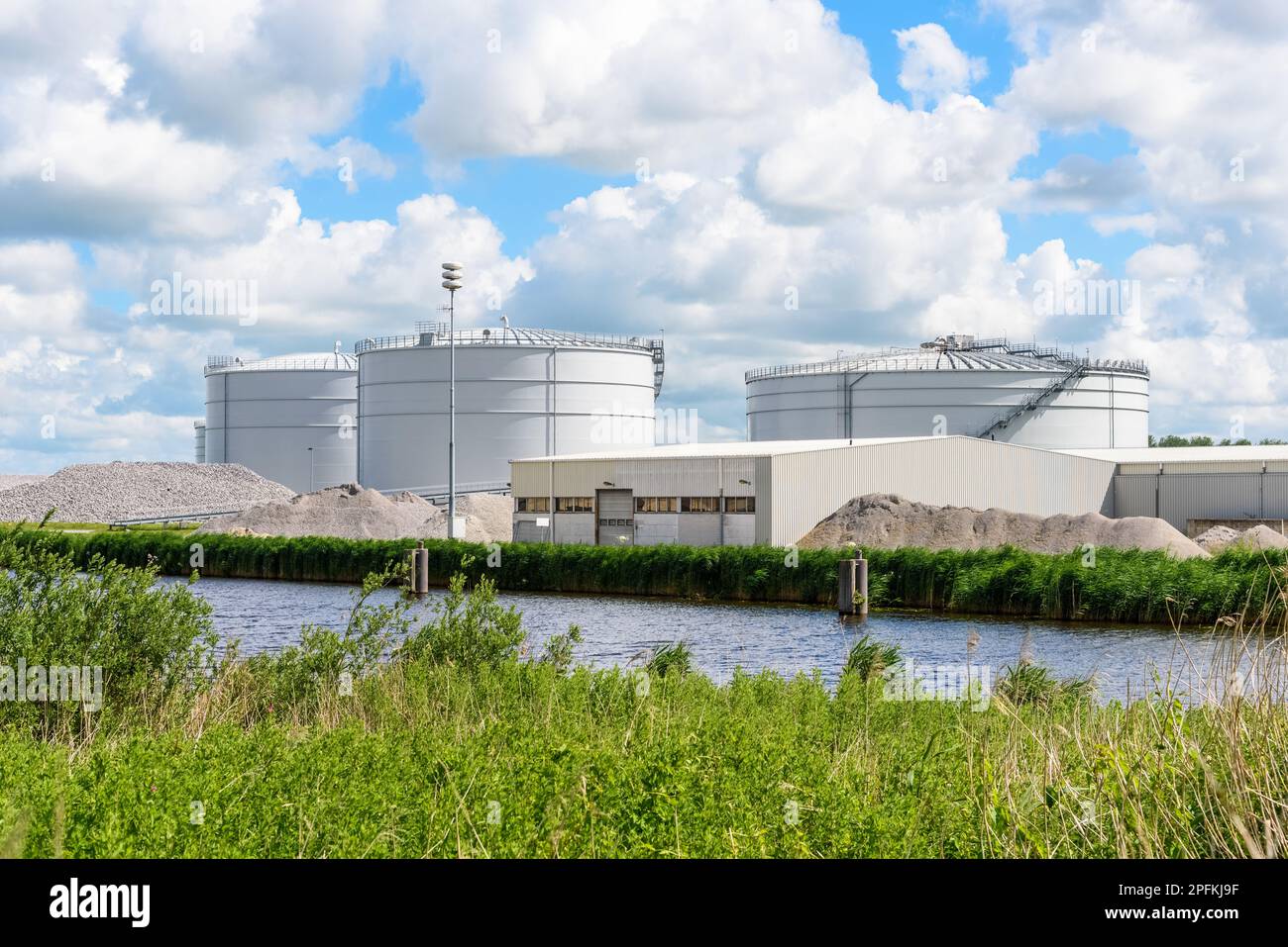 Usine de biogaz avec de grands digesteurs de biomasse le long d'un canal par une belle journée d'été Banque D'Images