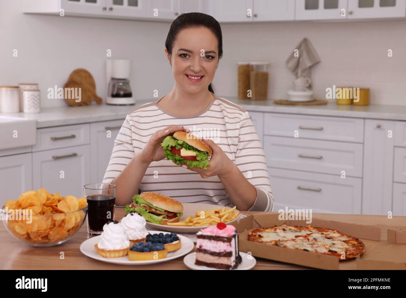 Bonne femme en surpoids avec des hamburgers et d'autres aliments malsains dans la cuisine Banque D'Images