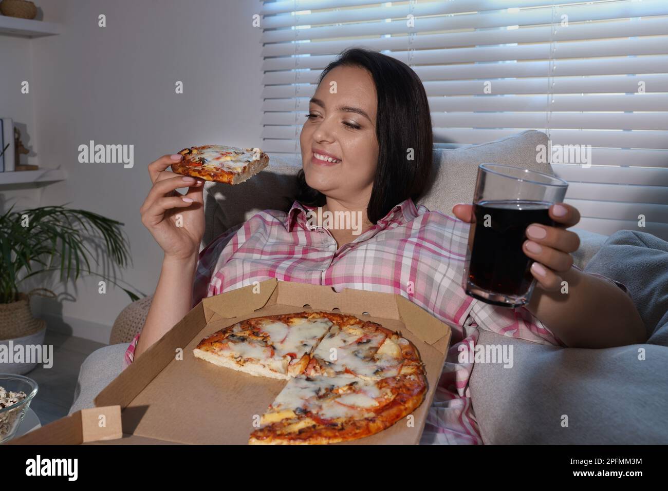 Bonne femme en surpoids avec pizza et cola sur le canapé à la maison Banque D'Images